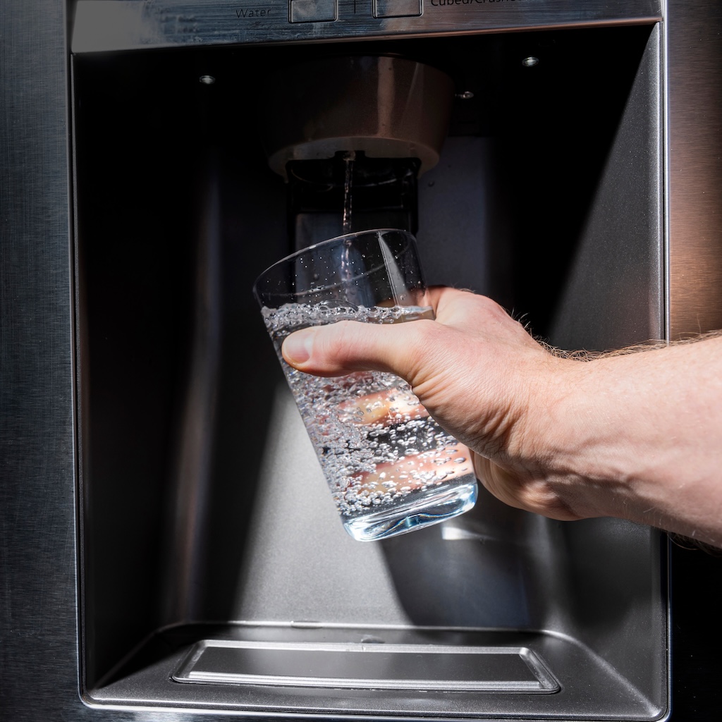 Home fridge dispenser filling glass held by male right hand point of view