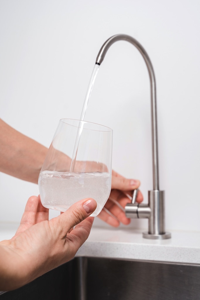 Woman get filtered water from stainless faucet into a glass.